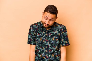 Latin kökenli genç adam bej arka planda izole edilmiş omuzlarını silkiyor ve gözleri açık..