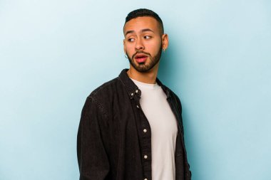 Mavi arka planda soyutlanmış genç bir İspanyol gülümsüyor, neşeli ve keyifli görünüyor..