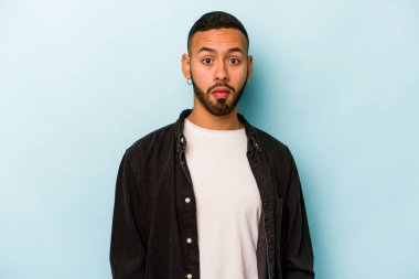 Genç İspanyol adam mavi arka planda izole edilmiş üzgün, ciddi yüz, mutsuz ve hoşnutsuz hissediyor.