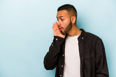 Mavi arka planda izole edilmiş genç İspanyol bir adam gizli bir sıcak fren haberi veriyor ve yana bakıyor.