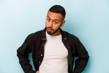 Mavi arka planda izole edilmiş genç bir İspanyol kafası karışmış, kuşkulu ve güvensiz hissediyor..
