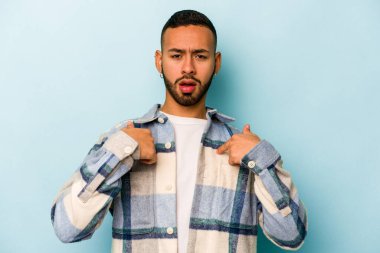 Mavi arka planda izole edilmiş genç İspanyol adam parmağını göstererek şaşırdı, geniş bir gülümsemeyle..