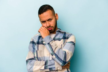 Genç İspanyol adam mavi arka planda izole edilmiş. Tekrarlanan bir görevden yorulmuş..