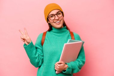 Genç beyaz bir kadın öğrenci pembe arka planda izole edilmiş neşeli ve kaygısız parmaklarıyla barış sembolü gösteriyor..