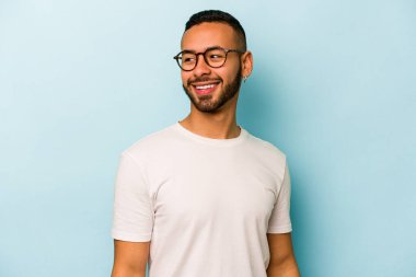 Mavi arka planda izole olmuş genç İspanyol adam gülüyor ve gözlerini kapıyor, rahatlamış ve mutlu hissediyor..