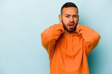 Genç İspanyol bir adam mavi arka planda izole edilmiş kafasının arkasına dokunuyor, düşünüyor ve bir seçim yapıyor..