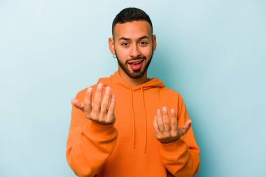 Genç İspanyol adam mavi arka planda izole edilmiş seni işaret ediyor sanki davet ediyormuş gibi..