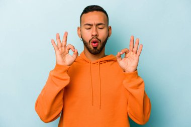 Mavi arka planda izole olmuş genç İspanyol adam sıkı çalışma gününden sonra rahatlıyor, yoga yapıyor..