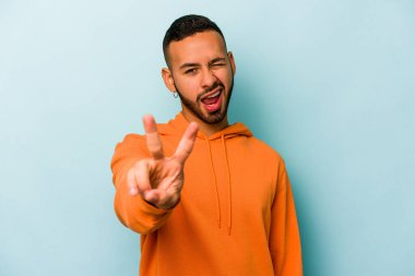 Mavi arka planda izole edilmiş genç İspanyol adam iki numarayı parmaklarıyla gösteriyor..