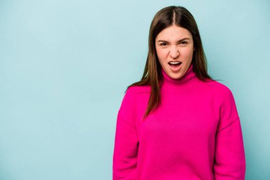 Kafkasyalı genç bir kadın mavi arka planda izole edilmiş çok kızgın, öfkeli, hayal kırıklığına uğramış bağırıyor..
