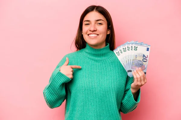 ピンクを背景に銀行券を持っている若い白人女性は シャツのコピースペースを指差す人 誇りと自信 — ストック写真