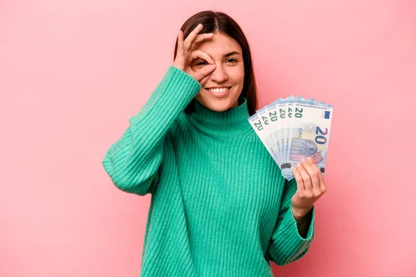 若いですCaucasian女性を保持銀行券隔離上のピンクの背景励起維持上のOkジェスチャー上の目 — ストック写真
