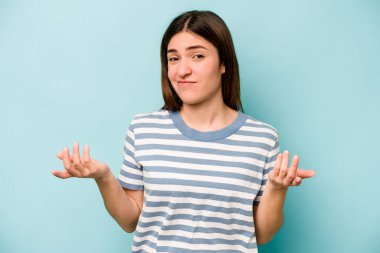 Kafkasyalı genç bir kadın mavi arka planda izole edilmiş sorgulama sırasında omuz silkiyor ve kuşkulanıyor..