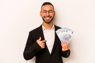 Latin kökenli genç bir adam, elinde banknotlar tutan, beyaz arka planda yaşayan, gömlek fotokopisini çeken, gururlu ve kendinden emin bir adam.