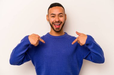 Beyaz arka planda izole edilmiş genç İspanyol adam parmağını göstererek şaşırdı, geniş bir gülümsemeyle..