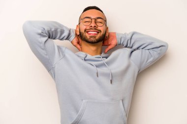 Beyaz arka planda izole edilmiş genç İspanyol bir adam kendini güvende hissediyor, elleri başının arkasında..