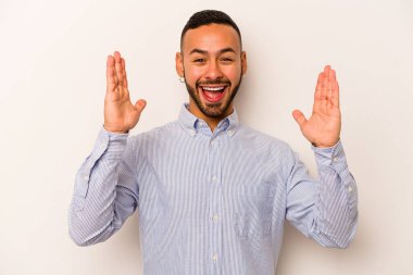 Latin kökenli genç bir adam beyaz arka planda izole edilmiş. Hoş bir sürprizle karşılaşıyor, heyecanlı ve el kaldırıyor..