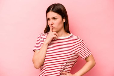 Pembe arka planda izole edilmiş genç beyaz kadın ya sır saklıyor ya da sessizlik istiyor..