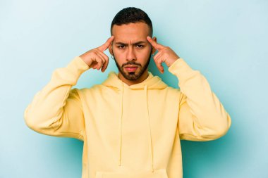 Mavi arka planda izole edilmiş genç İspanyol bir adam bir göreve odaklanmış, işaret parmaklarını işaret ediyor..