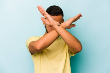 Genç İspanyol adam mavi arka planda izole edilmiş iki kolu çapraz tutuyor, inkar kavramı.