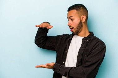 Mavi arka planda izole edilmiş genç İspanyol adam elleri arasında bir kopya alanı tutarken şok oldu ve hayrete düştü..