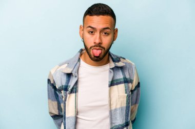 Genç İspanyol adam mavi arka planda izole edilmiş komik ve dost canlısı bir dil uzatıyor..