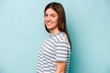 Kafkasyalı genç bir kadın mavi arka planda izole edilmiş. Kendine güvenen, ellerini kalçasında tutan..