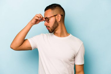 Genç İspanyol bir adam mavi arka planda izole edilmiş, başı ağrıyor, yüzüne dokunuyor..