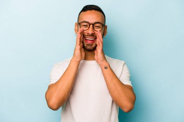 Genç İspanyol bir adam mavi arka planda izole edilmiş. Dedikodu yapıyor, bir şeyleri bildiriyor..