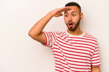 Beyaz arka planda izole edilmiş genç İspanyol adam uzaklara bakıyor ve elini alnına koyuyor..