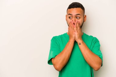 Genç İspanyol bir adam beyaz arka planda izole edilmiş. Düşünceli bir şekilde bir fotokopi odasına bakıyor. Ağzını eliyle kapatıyor..