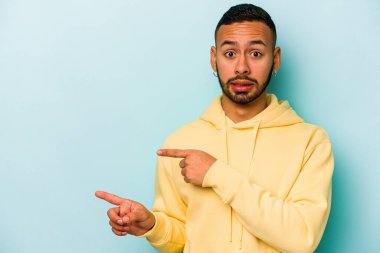 Mavi arka planda izole edilmiş genç İspanyol adam işaret parmağıyla fotokopi alanını işaret ederek şok oldu..