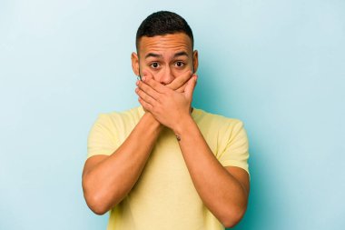 Genç İspanyol bir adam mavi arka planda izole edilmiş, ağzı kapalı ve elleri endişeli görünüyor..
