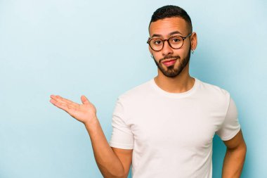 Mavi arka planda izole edilmiş genç İspanyol bir adam avucunun içinde bir fotokopi alanı ve belinde bir el daha gösteriyor..