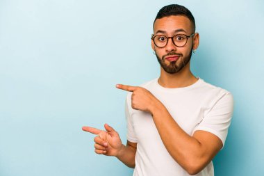 Mavi arka planda izole edilmiş genç İspanyol adam işaret parmağıyla fotokopi alanını işaret ederek şok oldu..