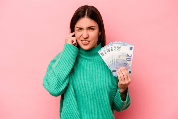手で耳をカバーピンクの背景に隔離された紙幣を保持若い白人女性 — ストック写真