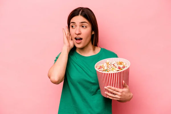 Giovane Donna Caucasica Possesso Popcorn Isolato Sfondo Rosa Cercando Ascoltare — Foto Stock