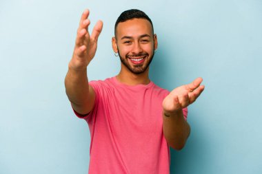 Latin kökenli genç bir adam mavi arka planda zaferi ya da başarıyı kutlarken şaşırmış ve şok olmuştu..