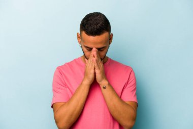 Genç İspanyol adam mavi arka planda izole edilmiş dua ediyor, bağlılık gösteriyor, dindar biri ilahi ilhamı arıyor..