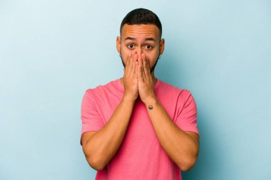 Genç İspanyol bir adam mavi arka planda izole edilmiş, ağzı kapalı ve elleri endişeli görünüyor..