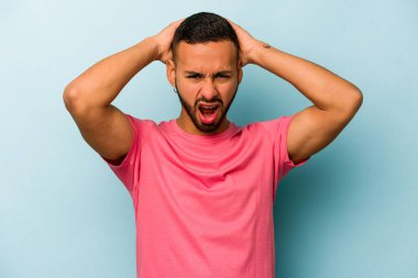 Genç İspanyol adam mavi arka planda izole edilmiş bağırıyor, çok heyecanlı, tutkulu, bir şeyden memnun..