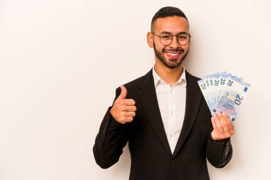 Genç İspanyol iş adamının elinde banknotlar var. Beyaz arka planda izole edilmiş. Gülümsüyor ve başparmağını kaldırıyor.