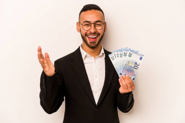 Latin kökenli genç bir iş adamı beyaz arka planda izole edilmiş banknotlar tutuyor. Hoş bir sürpriz alıyor, heyecanlı ve el kaldırıyor..