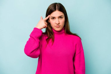 Mavi arka planda izole edilmiş genç beyaz kadın şakağı parmağıyla işaret ediyor, düşünüyor ve bir göreve odaklanıyor..