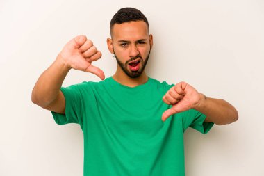 Beyaz arka planda izole edilmiş genç İspanyol adam baş parmağını aşağı gösteriyor ve hoşlanmadığını ifade ediyor..