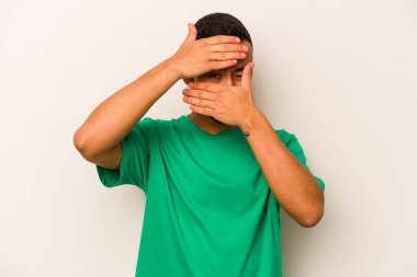 Beyaz arka planda izole edilmiş genç İspanyol adam kameraya parmaklarıyla göz kırpıyor, yüzünü kapatmaktan utanıyor..