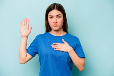 Beyaz bir kadın mavi arka planda izole edilmiş yemin ediyor, elini göğsüne koyuyor..