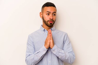 Latin kökenli genç bir adam beyaz arka planda izole edilmiş dua ediyor, bağlılık gösteriyor, dindar biri ilahi ilham arıyor..