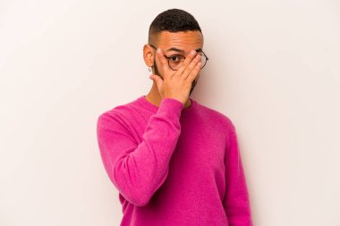 Beyaz arka planda izole edilmiş genç İspanyol adam parmaklarının arasından korkmuş ve gergin bir şekilde göz kırpıyor..