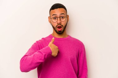 Beyaz arka planda izole edilmiş genç İspanyol adam parmağını göstererek şaşırdı, geniş bir gülümsemeyle..